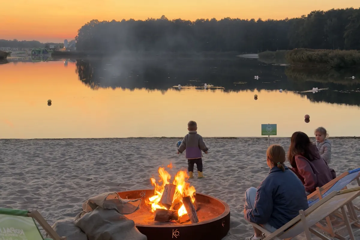 Ognisko na plaży Kopalni Wrocław o zachodzie słońca, leżaki przy palenisku nad jeziorem